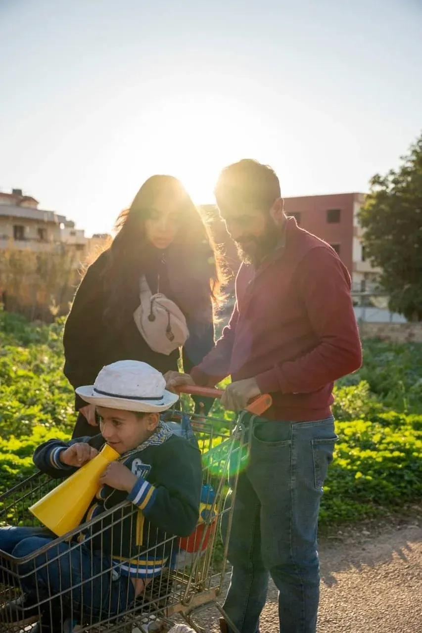 Man and woman leaning over a boy with a yellow megaphone in a shopping cart in a sunlit field